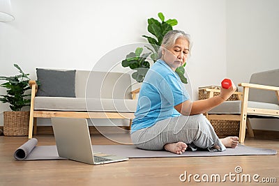 Asian senior woman lifting dumbbell for exercise and workout at home. Active mature woman doing stretching exercise in living room Stock Photo