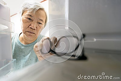 Asian senior woman with memory impairment symptoms,forget her glasses in the refrigerator or storing glasses in the fridge,female Stock Photo