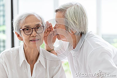 Asian senior woman holding hand near mouth telling funny,gossips on ears to friend,speaking in elderly woman ear and near face, Stock Photo