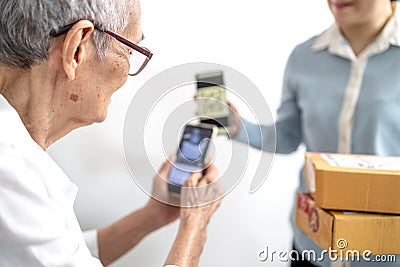 Asian senior woman receiving parcel post box from delivery service,paying deliver with smartphone to scan QR code payment purchase Stock Photo