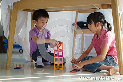 Asian sibling playing building block while sitting in a blanket fort in living room at home for perfect hideout away from their Stock Photo