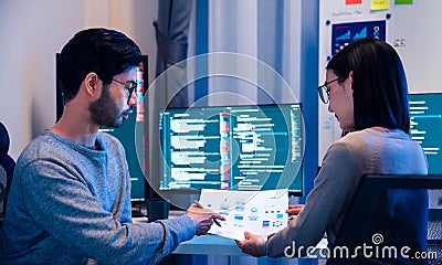 Asian software developers teams working on multiple screens displaying code and application diagrams at night in modern office Stock Photo