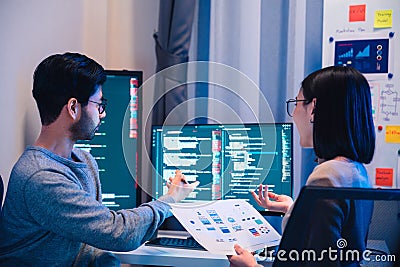 Asian software developers teams working on multiple screens displaying code and application diagrams at night in modern office Stock Photo