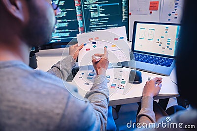 Asian software developers teams working on multiple screens displaying code and application diagrams at night in modern office Stock Photo