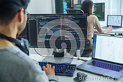 Asian software developers working on multiple screens displaying code and application diagrams in a modern office Stock Photo