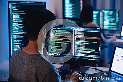 Asian software developers working on multiple screens displaying code and application diagrams at night in modern office Stock Photo