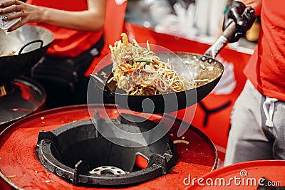 Asian street food festival in city. Chef cooking noodles and vegetables in a pan on fire. Fried chinese japanese noodles with Stock Photo