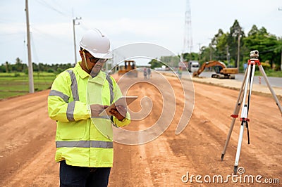 Asian surveyor engineer stands near levels telescope and used technology tablet to check detail of level in digital drawing to Stock Photo
