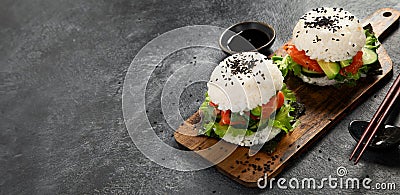 Asian sushi burger, soy sauce, chopstick on dark background. Trendy hybrid food Stock Photo