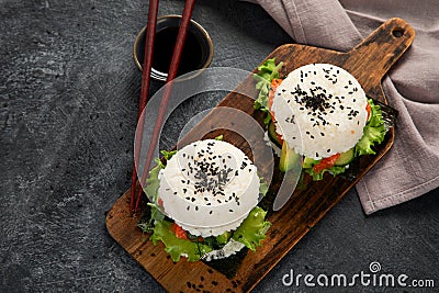 Asian sushi burger, soy sauce, chopstick on dark background. Trendy hybrid food Stock Photo