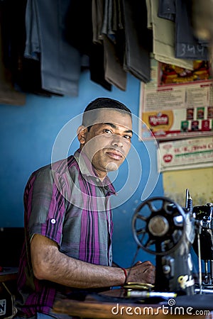 An Asian tailor work on the sewing machine, clothes hang on top. Editorial Stock Photo