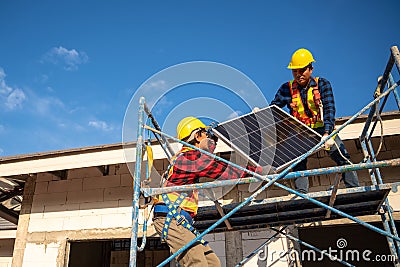 Asian technicians or workers wearing fall protection safety clothing carry solar cells to install on the roof of a house. Concept Stock Photo