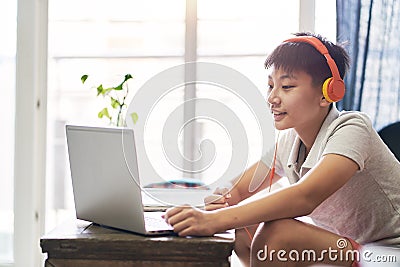 Asian teenage boy studying at home wearing headset and smiling Stock Photo