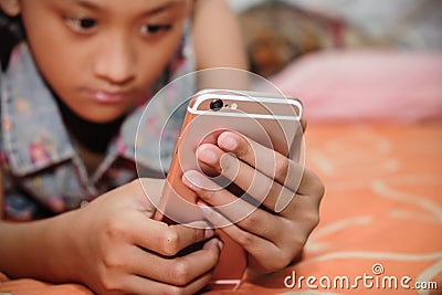 Asian Teenage Girl Focus Playing Her Smartphone While Resting on Bed Stock Photo