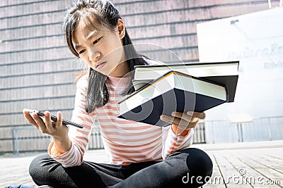 Asian teenage schoolgirl with a books and mobile phone in her hand,female student choosing between study and play,woman is Stock Photo