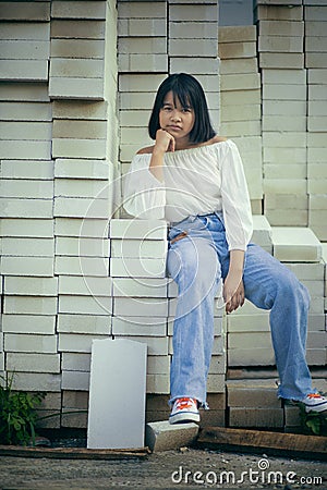 Asian teenager sitting on stack of contruction brick Stock Photo