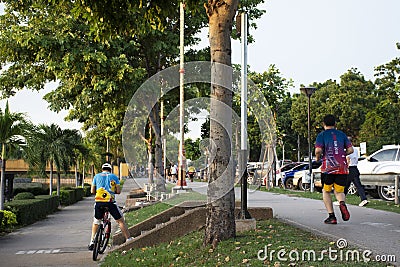 Asian thai people and foreign travelers walking jogging exercise biking bicycle on pathway around pondside in dusk time at Nong Editorial Stock Photo