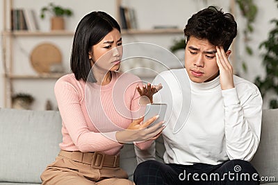 Asian Wife Showing Cheating Husband His Phone Suspecting Affair Indoors Stock Photo