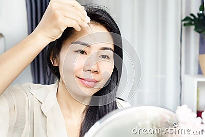 Asian woman age 40s applying serum collagen on her skin face, forehead for anti-aging and winkles Stock Photo