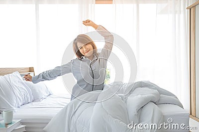 An Asian woman aged about 20 wakes up in the morning in a bright bed in a bedroom or hotel After a restful night`s sleep Stock Photo