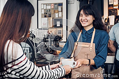 Asian woman barista wear jean apron holding coffee cup served to Stock Photo