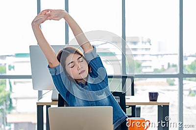 Asian woman creative designer stretching arms up from working with laptop in modern office.take a break from work Stock Photo