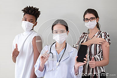 Asian woman doctor holding showing smart phone and syringe with mask and stethoscope. Vaccinated people standing back Stock Photo