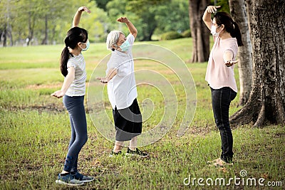 Asian woman is doing exercise activity for the old elderly and child girl,family workout,wearing protective mask outdoor at park, Stock Photo