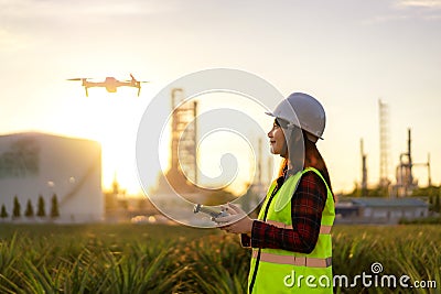 Asian woman engineer operate flying drone over oil refinery plant during sunrise building site survey in civil engineering project Stock Photo