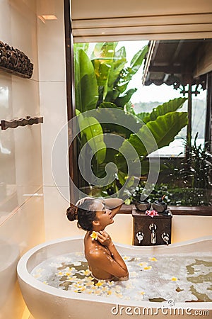 Asian woman enjoying in flower spa bath with foam, bubbles and yellow flowers Stock Photo