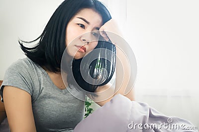 Asian woman feeling sad and depressed sitting in bed next to the window Stock Photo