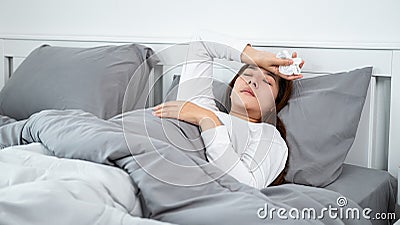 Asian woman feeling sick and sleeping in blanket on the bed while holding tissue in hands and touching forehead Stock Photo