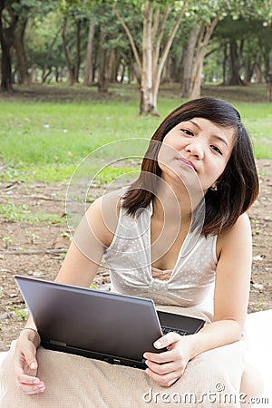 Asian woman flagging with laptop sitting at park Stock Photo