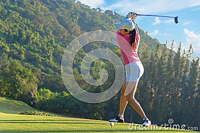 Asian woman golf player doing golf swing tee off on the green evening time, she presumably does exercise. Stock Photo