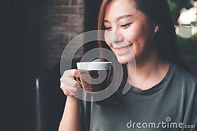 An Asian woman holding and drinking hot coffee with feeling good in vintage cafe Stock Photo