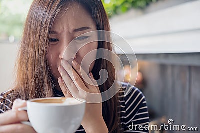 Asian woman holding hot coffee with feeling strange and smelling bad in coffee shop Stock Photo