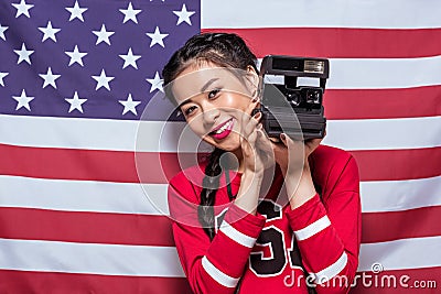 Asian woman holding retro photo camera with american flag behind Stock Photo