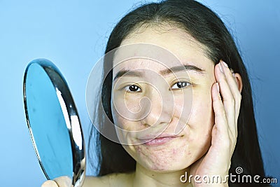 Asian woman looking at herself in the mirror, Female feeling annoy about her reflection appearance show the aging facial. Stock Photo