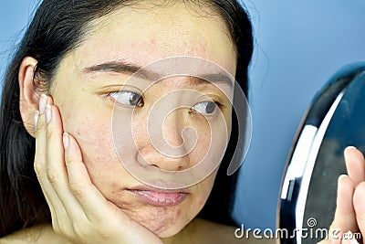 Asian woman looking at herself in the mirror, Female feeling annoy about her reflection appearance show the aging facial skin sign Stock Photo