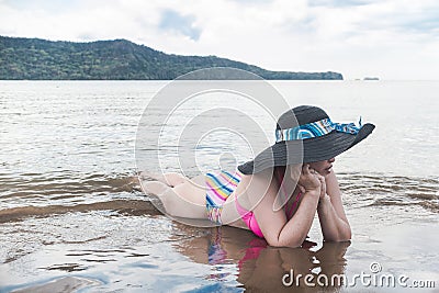 An asian woman lying in the sand and shallow waters at the beach. In deep thought, soul searching or contemplation. Wearing a Stock Photo