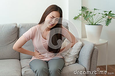 Asian woman with menstruation and pain period cramps. young women having painful sitting on sofa at her home Stock Photo