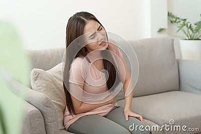 Asian woman with menstruation and pain period cramps. young women having painful sitting on sofa at her home Stock Photo