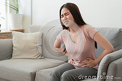 Asian woman with menstruation and pain period cramps. young women having painful while sitting on sofa at her home Stock Photo