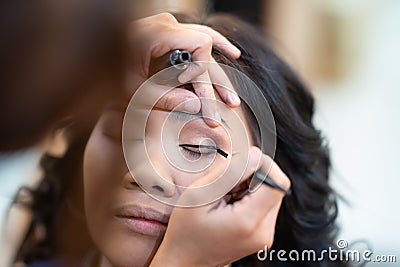 Asian woman model false eyelashes during make-up session. The make-up artist is applying a black eyeliner with the brush on eyelid Stock Photo