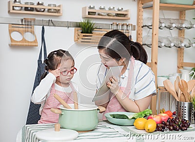 Asian woman mother and daughter play together in kitchen,mom hold tablet for teach little girl how to cook in semester break, Stock Photo