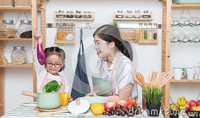 Asian woman mother and daughter play together in kitchen,mom hold tablet for teach little girl how to cook in semester break, Stock Photo
