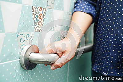 Asian woman patient use toilet support rail in bathroom, handrail safety grab bar, security in nursing hospital Stock Photo