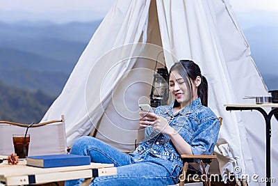 Asian woman reading book while on a solo trekking camp on the top of the mountain with small tent for weekend activities and Stock Photo