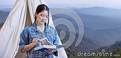 Asian woman reading book while on a solo trekking camp on the top of the mountain with small tent for weekend activities and Stock Photo