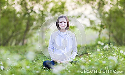Asian woman is relaxingly practicing meditation yoga in the forest full of daisy flower in summer to attain happiness from inner Stock Photo